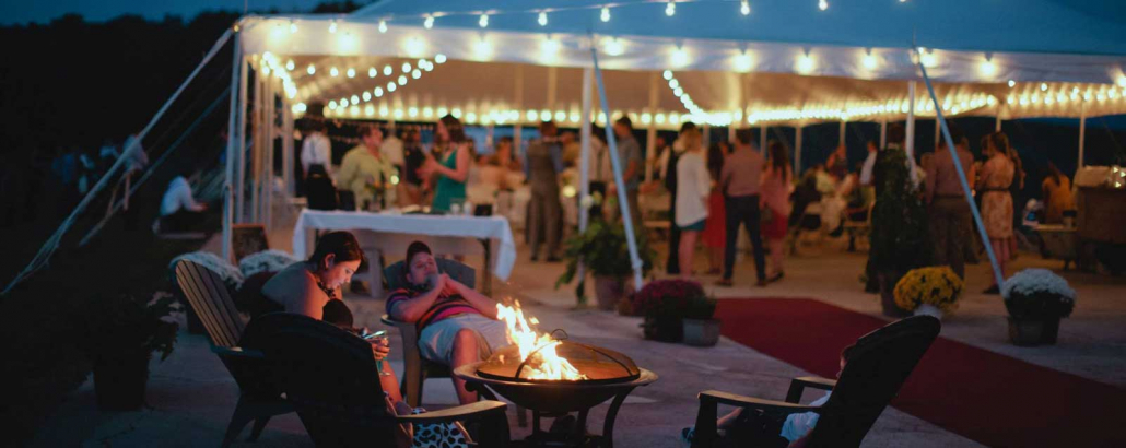Outdoor event at On Sunny Slope Farm, featuring a tent with string lights, guests mingling, and a cozy fire pit with seating, creating a warm and inviting atmosphere for private gatherings.
