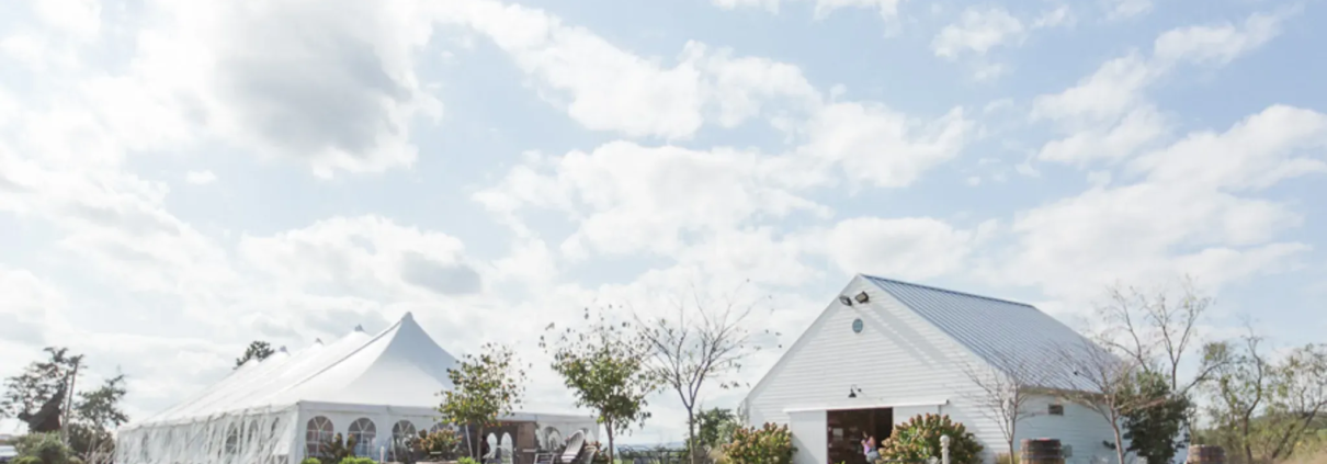 Outdoor venue with a white tent and barn under a blue sky.