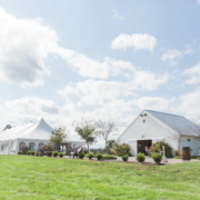Outdoor venue with a white tent and barn under a blue sky.