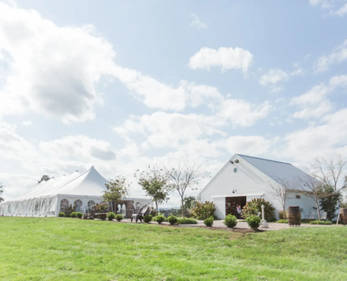 Outdoor venue with a white tent and barn under a blue sky.